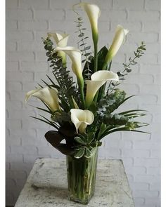 a vase filled with white flowers sitting on top of a stone table next to a brick wall