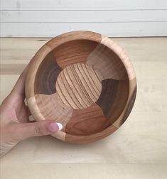 a hand holding a wooden bowl on top of a table next to a white wall