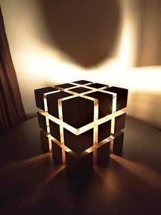 an illuminated cube sitting on top of a table next to a curtained window with the light coming through it