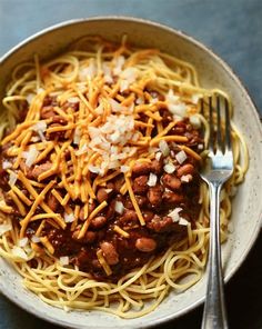 a white bowl filled with spaghetti and meat covered in cheese on top of a table