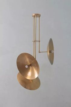 an overhead light fixture with two large brass discs hanging from it's side and one circular metal object in the middle