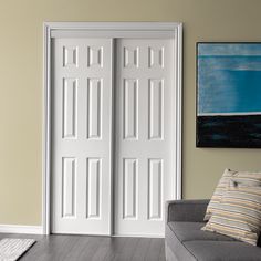 a living room with two white doors and a gray couch in front of the door