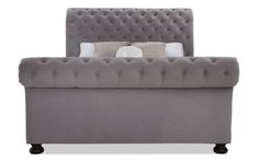 a gray bed with pillows on it and a white pillow behind the headboard,