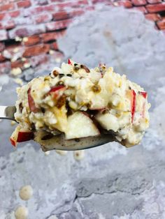 a spoon full of food sitting on top of a brick wall covered in toppings