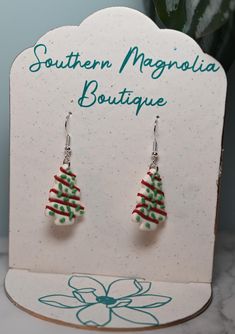 christmas tree earrings with red, green and white beads on the bottom are sitting in front of a sign