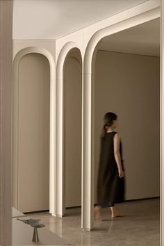 a woman walking through an empty room with arches and columns on either side of her