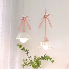 two hanging lights with bows on them hang from the ceiling above a plant in a vase