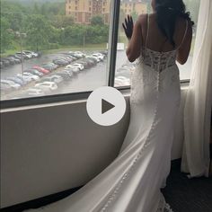 a woman in a white wedding dress looking out a window at the parking lot outside