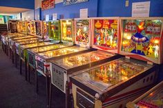 a row of pinball machines in a room with blue walls and carpeted flooring