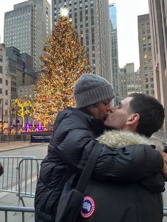 a man and woman kissing in front of a large christmas tree with lights on it