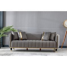 a grey couch with gold trim and pillows in front of a striped wall behind it