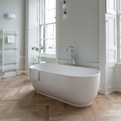 a white bath tub sitting on top of a hard wood floor next to two windows