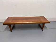 a wooden coffee table sitting on top of a cement floor next to a white wall