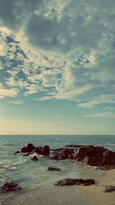 an empty beach with rocks and water under a blue sky filled with wispy clouds