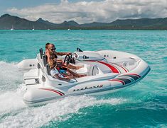 a man and woman riding on the back of a white boat in clear blue water