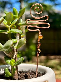 a small plant in a white pot with a spiral wire decoration on it's top