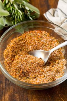 a glass bowl filled with seasoning on top of a wooden table next to herbs