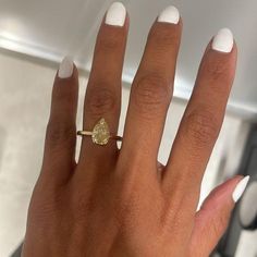 a woman's hand with white nails and a gold ring on her left hand