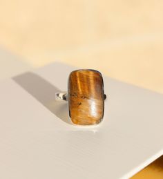 A stone like no other, the Tiger's Eye semi-precious stone is the focus of this fabulous ring. A bold, rectangle cut of the Tiger's Eye stone sits in a sterling silver case and band. Due to the natural elements found within the Tiger's Eye stone, each ring reflects its own array of warm mustard and brown tones.   Available in three sizes; US ring size 8, 9, & 10. Store in a safe place to avoid scratching. Clean carefully with a jewellery polishing cloth.