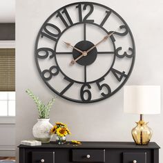 a large clock on the wall above a table with flowers and vases in front of it