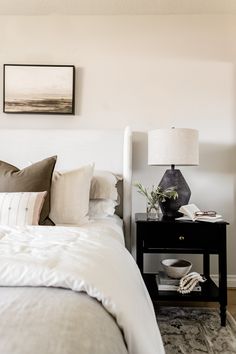 a bed with white sheets and pillows in a bedroom next to a painting on the wall