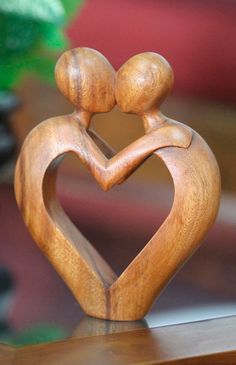 a wooden sculpture of two people holding each other's hands in the shape of a heart