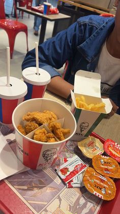 a table topped with two buckets of fried food and cups of soda on top of it