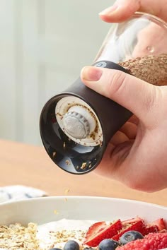 a person pouring granola into a bowl with berries and blueberries