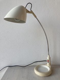 a white desk lamp sitting on top of a wooden table next to a white wall