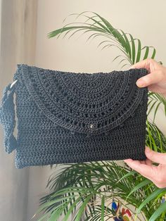 a crocheted purse being held up by a woman's hand in front of a potted plant