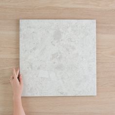 a person's hand pointing at a white marble tile