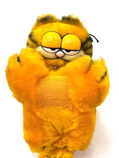 a stuffed animal that is yellow and has eyes on it's face, with one hand in the air