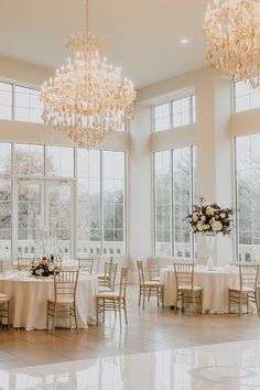 a room filled with lots of tables covered in white tablecloths and chandeliers