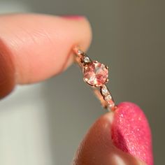 a close up of a person's finger holding a ring with a pink diamond