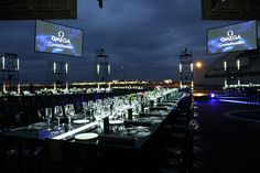 a long table with wine glasses and place settings in front of large screen screens at night