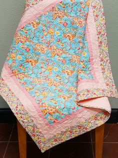 a blue and pink quilted blanket sitting on top of a wooden chair next to a wall