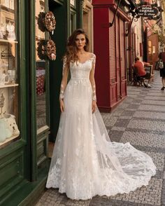 a woman standing in front of a store wearing a white wedding dress with long sleeves