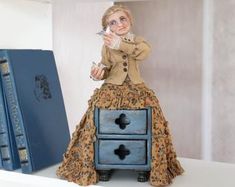 a doll is sitting on top of a dresser with books behind her and holding a knife