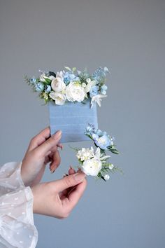 two hands holding flowers in front of a blue box with white and blue flowers on it