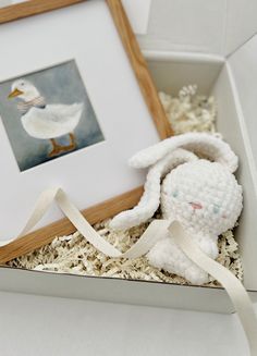 a white stuffed animal sitting inside of a box next to a framed photo and ribbon