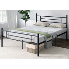 a black metal bed frame with white sheets and pillows on top of it, next to a potted plant