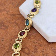 Estate/ vintage 14KT yellow gold Byzantine design, textured + cabochon, multi-gemstone link bracelet. Textured, shiny, and matte finishes on this piece. Slightly concave pieces with cabochon, amethyst, blue topaz, garnet, peridot, and citrine oval gemstones. Each gemstone measures: 7mm x 5mm; (8) total Rectangle byzantine + shiny open design links bracelet Measures 7.5", but fits shorter when clasped at the shorter length Weight: 22 grams Measures: 10mm wide Secure snap clasp Stamped 14K Great v Gold Jewelry With Gemstone Accents In Oval Cabochon, Gold Jewelry With Gemstone Accents And Oval Cabochon, Gold Jewelry With Gemstone Accents, Elegant Multicolor Bracelet With Cabochon, Elegant Multicolor Cabochon Bracelets, Elegant Multicolor Cabochon Bracelet, Gold Multi-stone Oval Cabochon Jewelry, Gold Oval Cabochon Multi-stone Jewelry, Gold Oval Bracelet With Bezel Setting