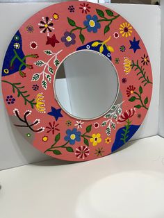 a pink toilet seat with colorful flowers painted on the front and sides, sitting next to a sink