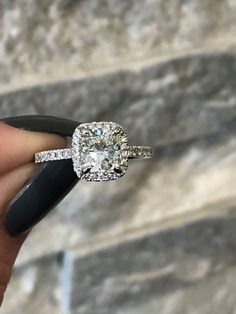 a woman's hand holding an engagement ring in front of a stone wall and black nail