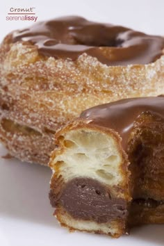 two chocolate covered doughnuts sitting on top of a white plate next to each other