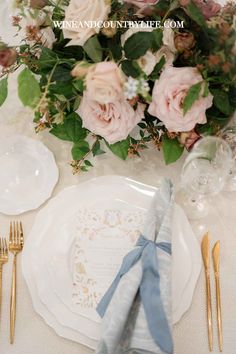 the table is set with white plates and silverware, gold cutlery, and pink flowers