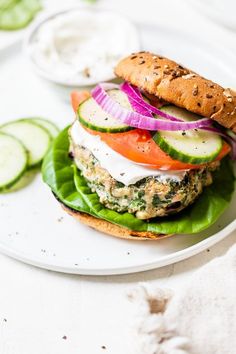 a sandwich with cucumber, tomato, onion and lettuce on a white plate