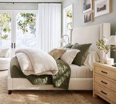 a white bed sitting in a bedroom next to a window covered in green and white blankets