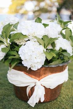 a flower pot with white flowers and greenery on the grass in an outdoor setting