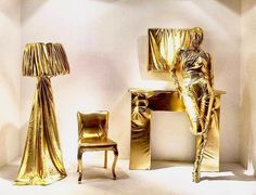 two golden chairs and a gold lamp are on display in front of a white wall